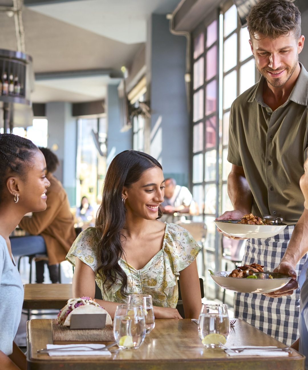 Group Of Female Friends Meeting Up In Restaurant Being Served Meal By Waiter